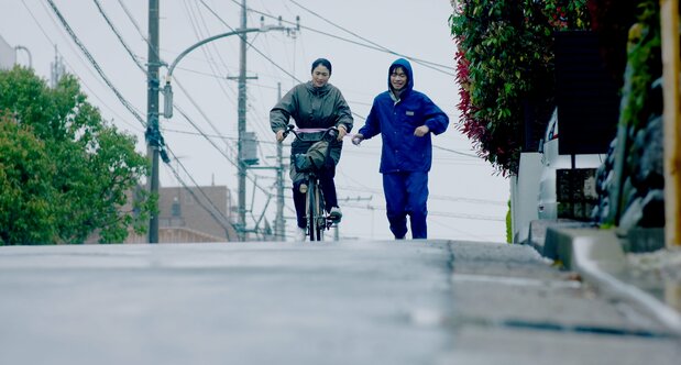 智の運動療法を助けるため、自転車で伴走する令子 ©THRONE / KARAVAN Pictures