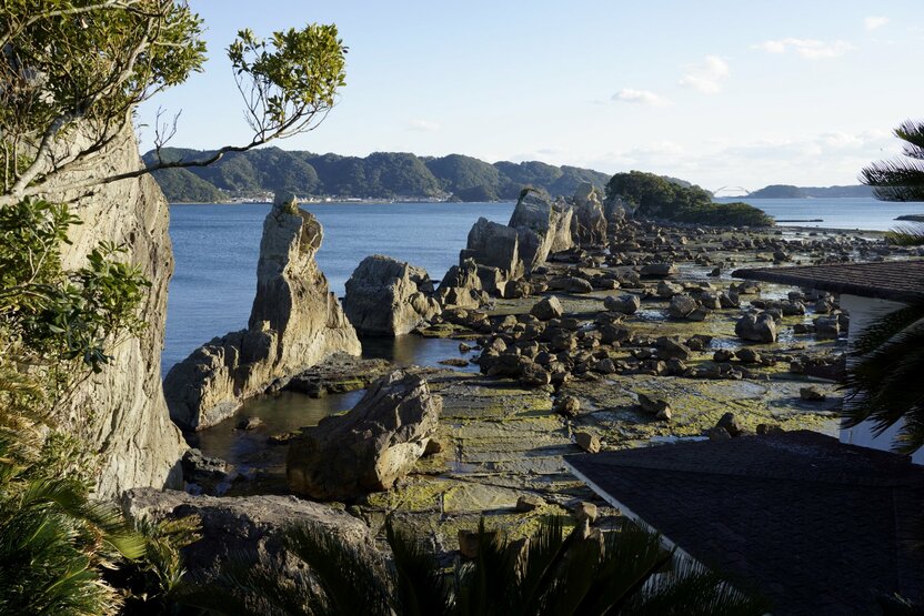 一列に並ぶ岩の奥、緑に覆われた弁天島（中央右）には鳥居と祠がある　撮影＝大坂 寛