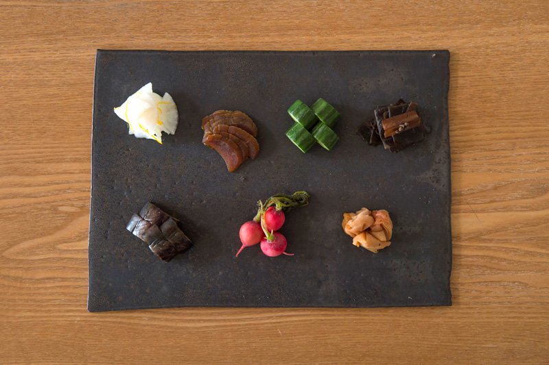 En haut à partir de la gauche : navet aromatisé au yuzu, narazuke (gourde fermentée au saké), asanukazuke (fermentation légère au son de riz) de concombres, tsukudani de kombu (algue kombu longuement mijotée avec de la sauce de soja et du sucre). En bas à partir de la gauche : asanukazuke d’aubergines, petit radis, umeboshi
