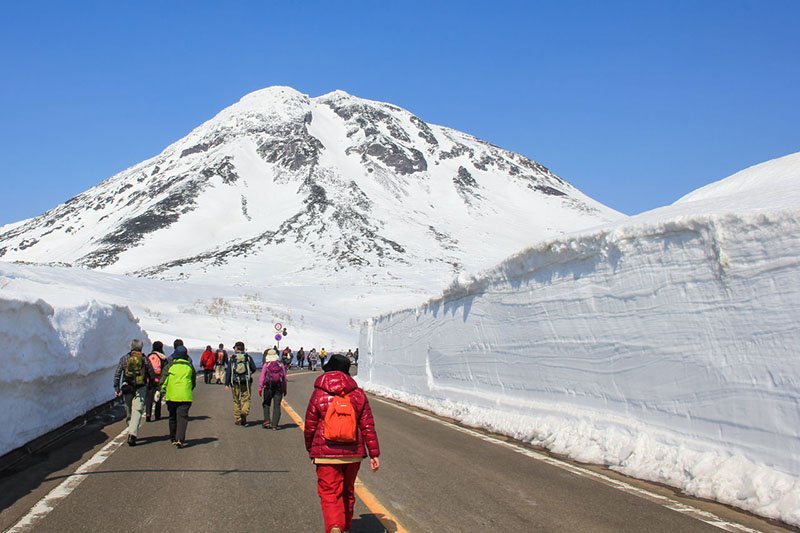 Personas marchando entre las paredes de nieve de Shiretoko mientras contemplan las nieves plateadas de Rausudake. Foto cortesía de Asociación de Turismo de Shiretoko Shari-chō.