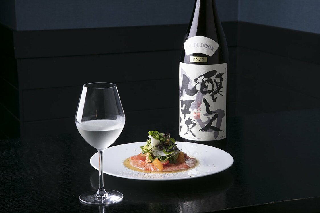 鮭魚片配上貝比生菜、柑橘和草莓，製成鮭魚「卡帕奇歐」，佐以用酒米「山田錦」釀製的「釀人九平次EAU DU DESIR純米大吟釀 山田錦2016」。「EAU DU DESIR」在法語中意為「希望之水」