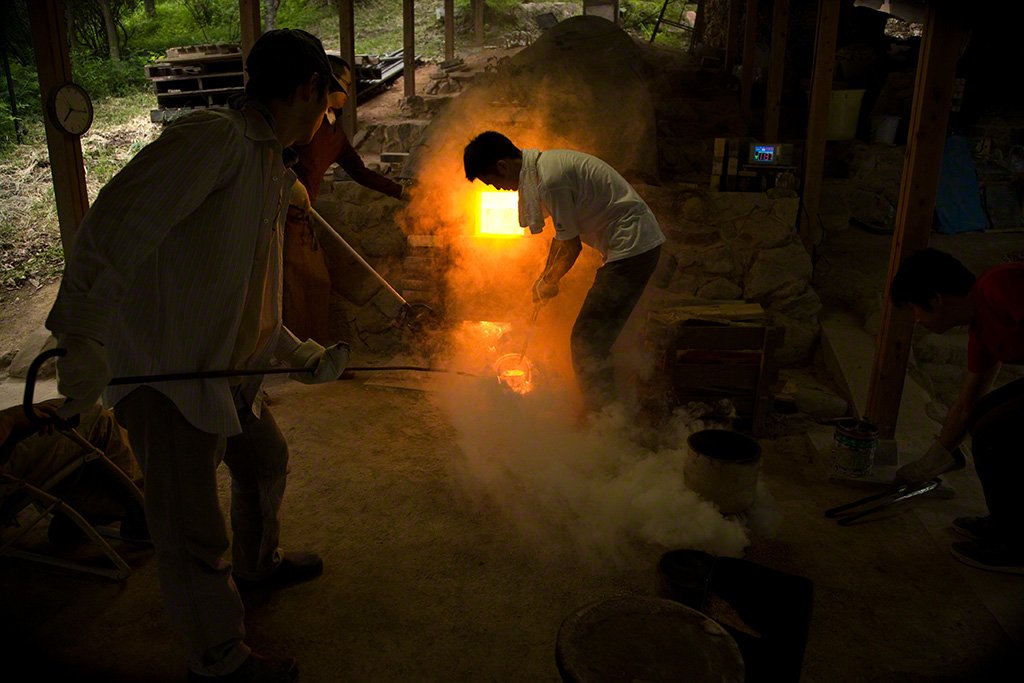 Wood is added and clay creations near the opening of the kiln are taken out and checked.