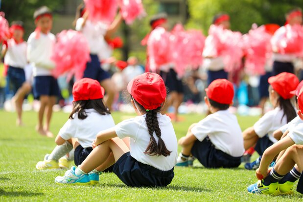 Niños de primaria sentados en la postura taiiku zuwari, que se utiliza en los patios o gimnasios escolares. (PIXTA)