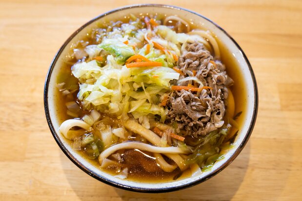 Udon de Yoshida servido con col y carne de caballo, sazonado con suridane, un condimento que tiene como base chile rojo. Para saborear todavía más la firmeza de los fideos se recomienda el plato tsukemen, en el que el udon y el caldo se sirven por separado.