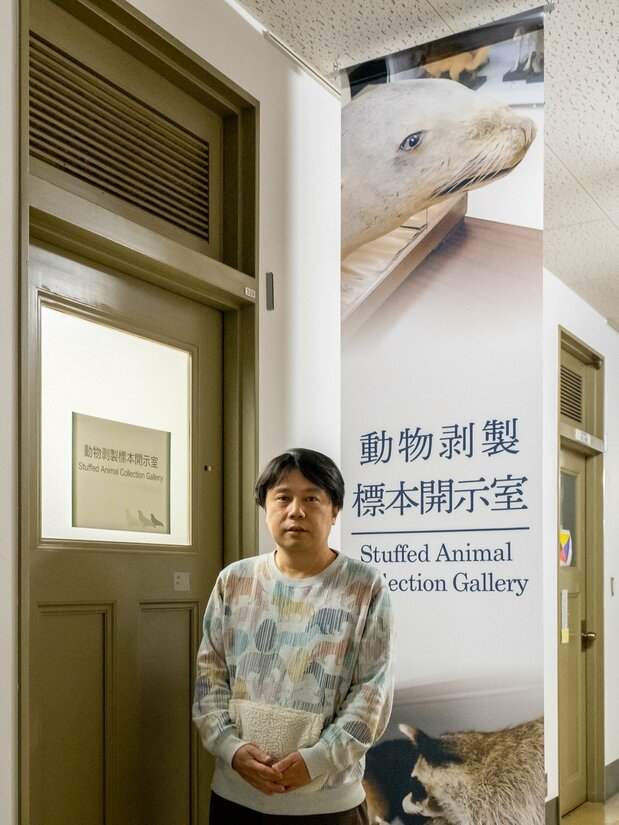 El profesor asociado Maruyama Munetoshi, del Museo de Investigación Integrada de la Universidad de Kyūshū, junto a un cartel con la fotografía del león marino japonés, en la entrada de la galería de especímenes de taxidermia. (© Michiko Hayashi)