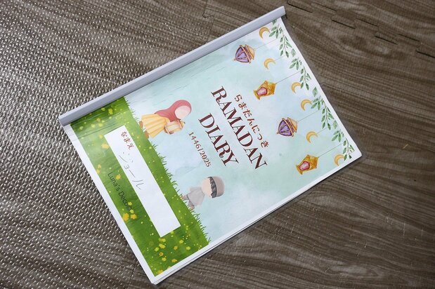 ابتكرت عائشة ”كتاب رمضان“، حيث يمكن للأطفال تسجيل يومياتهم الرمضانية، مما يساعدهم على توثيق تجربتهم والتفاعل مع أجواء الشهر الكريم بطريقة ممتعة ومفيدة. (© نومورا كازويُكي)