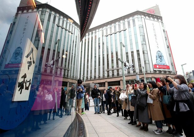 Shoppers in the Ginza district of Tokyo snap commemorative photos of a sign announcing the new era name in a shop window on April 1, 2019. (© Jiji)