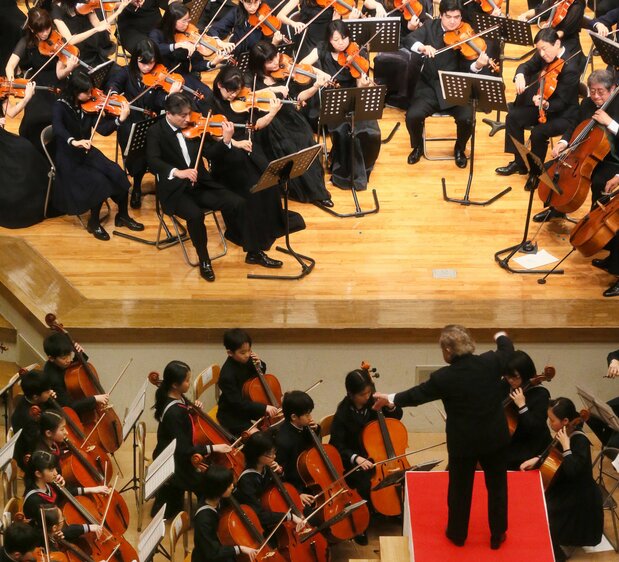 Naruhito, encore prince héritier (deuxième à droite sur l’estrade), joue du violon dans le même orchestre que sa fille Aiko, au violoncelle (quatrième à gauche sur la dernière rangée gauche en bas de l’estrade), lors d’un concert à l’établissement Gakushûin en avril 2013 (Jiji)