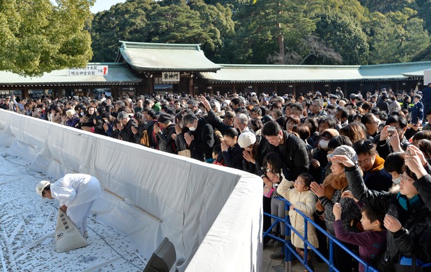Visitors crowd around the main hall at the Meiji Shrine to offer up their first prayer of the New Year, while a staff member gathers money tossed into the collection area. (© Jiji)