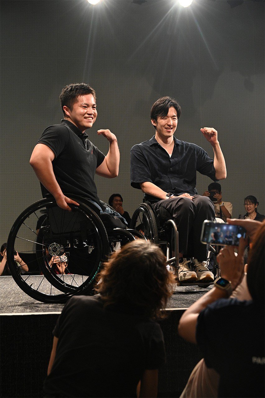 【高校生作品】私服姿の車いすラグビー日本代表の橋本さん（左）と中町さん（右）。撮影した大里さんは「カメラに向かって微笑む2人と、歓声を上げるファンを一緒に撮ることで、2人がたくさんの人に応援されていることを表現した」