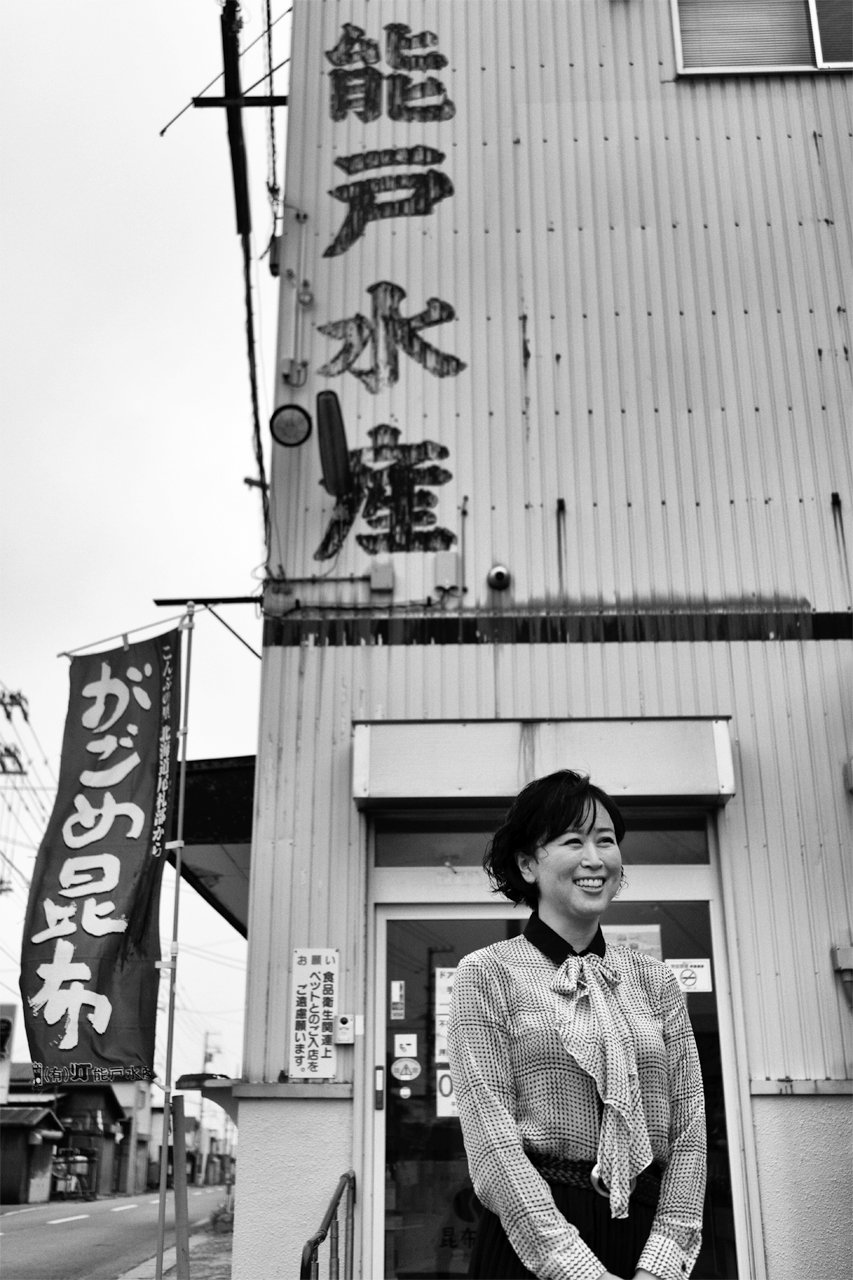 がごめ昆布の幟（のぼり）がはためく昆布村の店舗前に立つ能戸さん（2021）
