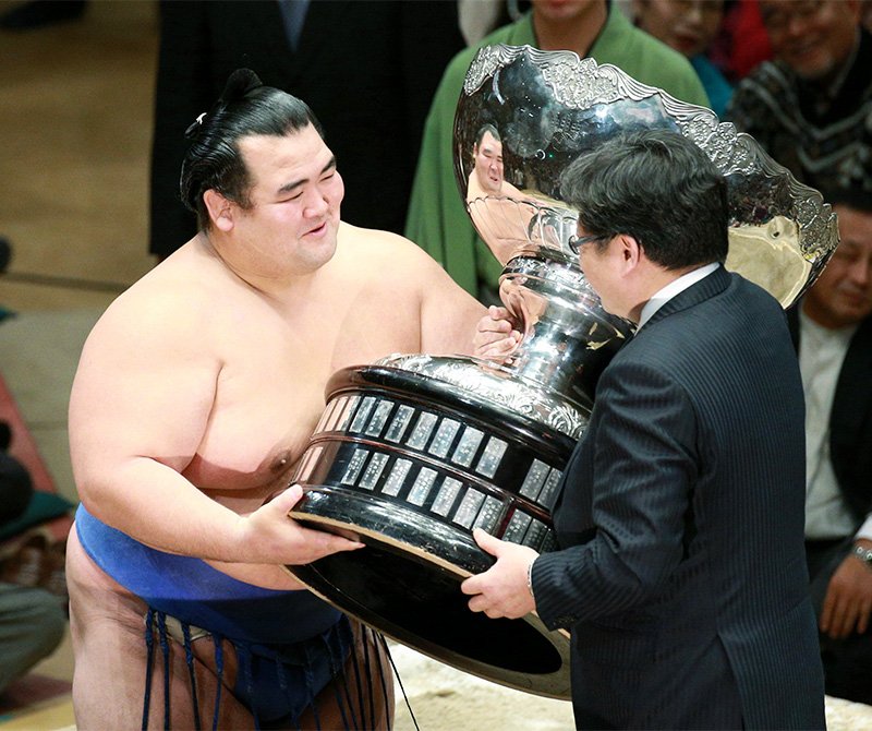Kotoshōgiku (izquierda) recibe el Trofeo del Primer Ministro en el Pabellón de Sumō de Ryōgoku el 24 de enero de 2016. (© Jiji)