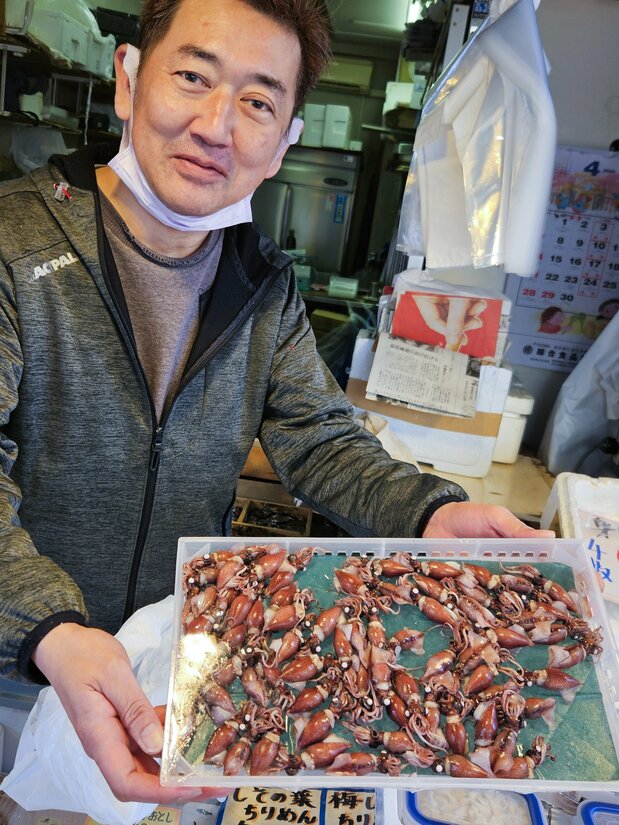筑地场外市场的鲜鱼店工作人员端着一盘富山产的饱满荧光鱿（笔者摄影）