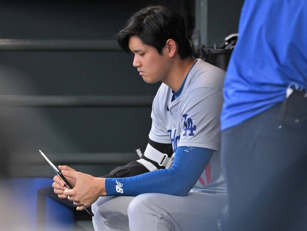 米大リーグのロッキーズ戦のベンチで、タブレット端末を見るドジャースの大谷翔平=2024年6月18日、デンバー(時事)
