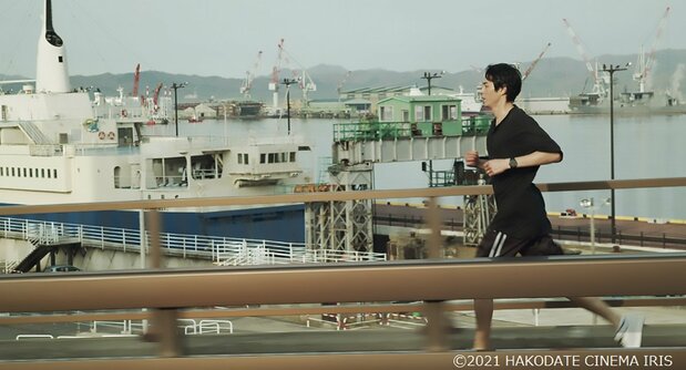 和雄は摩周丸を横目にともえ大橋を走る（『草の響き』より）©2021 HAKODATE CINEMA IRIS