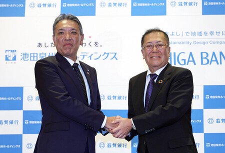 Shiga Bank President Shinya Kubota (right) and Senshu Ikeda Holdings President Hirohito Sakaguchi shake hands after a joint press conference held in the city of Osaka on Thursday to announce the two entities' basic agreement to aim for their April 2028 business integration.