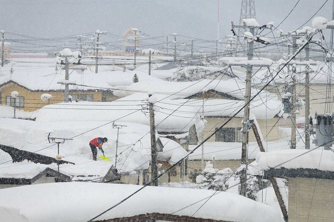 Una persona retira la nieve de un tejado en Yuzawa (Pixta).