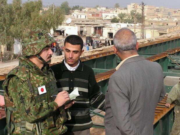 El Coronel de la Fuerza Terrestre de Autodefensa Satō Masahisa, comandante de la misión japonesa de reconstrucción en Irak, habla con representantes locales sobre el estado de un puente cerca de Samawah el 26 de enero de 2004. (© Jiji)