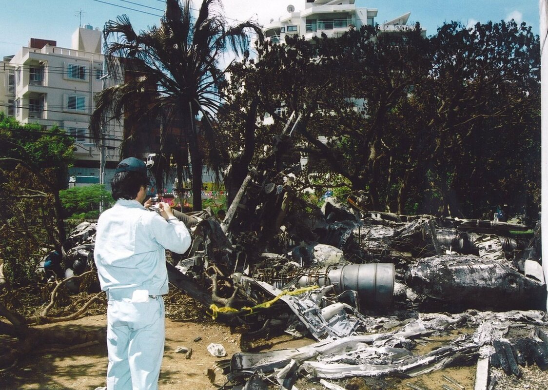 沖縄国際大学本館の南側壁付近に散らばった米軍ヘリコプターの残骸を調べる日本側当局者＝2004年8月15日、宜野湾市の同館構内（時事）