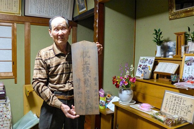 平井数馬の兄・平井幸三郎の孫の幸治氏。右は数馬の祭壇。手にしているのは台中州北斗街にあった幸三郎の家の棟札