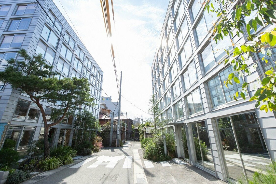 ガラス張りの社屋ビル2棟が建つ路地の奥にはワーキングスペースの古民家が並ぶ。