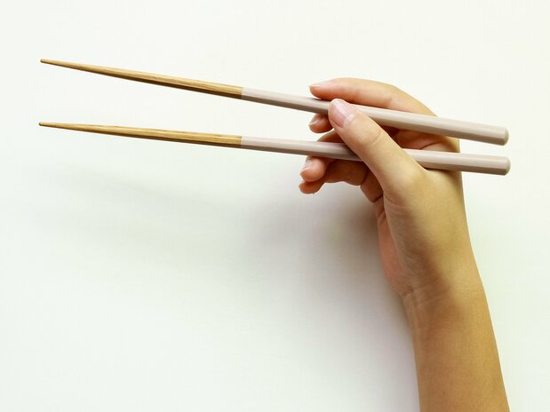 Prendre la baguette du haut entre le pouce et l’index comme on tiendrait un crayon. Intercaler la baguette du bas à la base du pouce et maintenir avec l’annulaire. (Pixta)