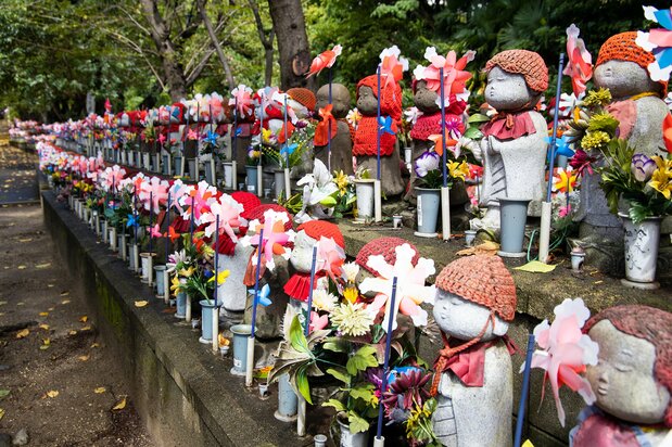 Pinwheels and offerings of flowers and toys decorate the rows of Jizō statues.