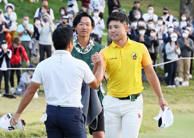 日本オープンゴルフ最終日、18番をホールアウトし、2位の比嘉一貴(左)と健闘をたたえ合うアマチュアの蝉川泰果(右)=2022年10月23日、兵庫・三甲GCジャパン(時事)