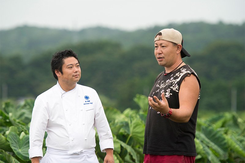 開店前、その日に使う野菜をファーム白石に仕入れに行く。野菜の状態を語る白石さん（右）と萩さん