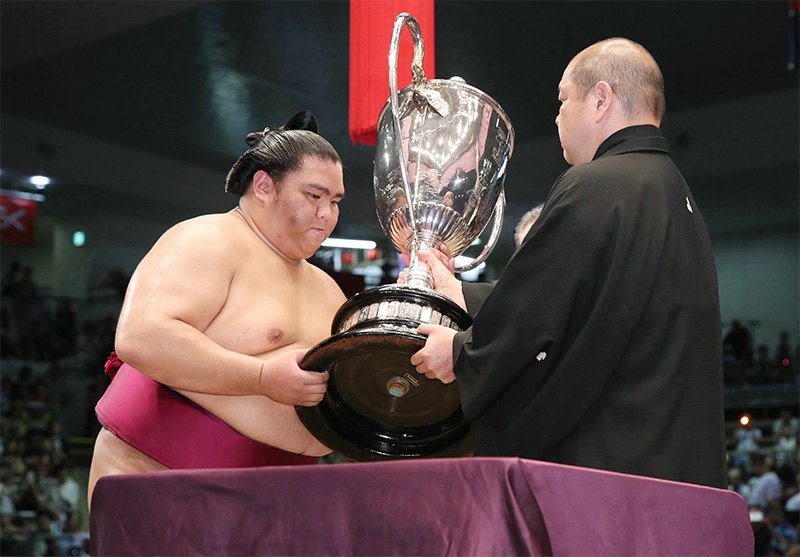 Mitakeumi (left) receives the Emperor’s Cup from Japan Sumō Association Chairman Hakkaku at Dolphins Arena in Nagoya, Aichi Prefecture, on July 22, 2018. (© Jiji)