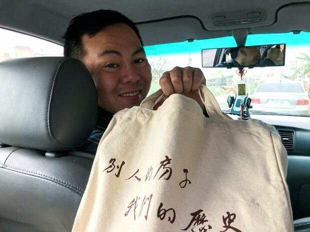 張敬業さんが手に持つのは「鹿港囝仔」が制作したエコ・バッグとそこに印字された「別人的房子,我們的歴史」の文字(筆者撮影)