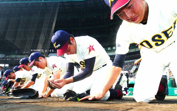 Players from Aomori Prefecture’s Hachinohe Gakuin Kōsei High School shed tears as they gather dirt from the infield at Kōshien after a second-round loss to Aichi Prefecture’s Tōhō High at the 2016 summer tournament. (© Jiji)